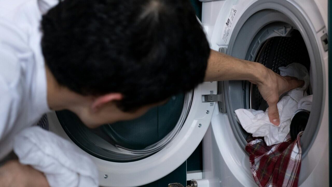 Close-up of a man placing clothes into a washing machine during household chores.