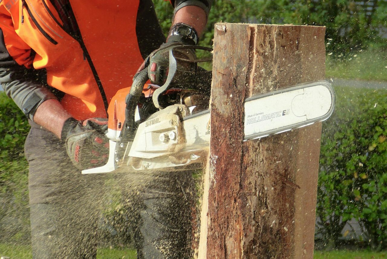 Lumberjack using a chainsaw to cut a tree trunk outdoors, showcasing professional equipment and safety gear.