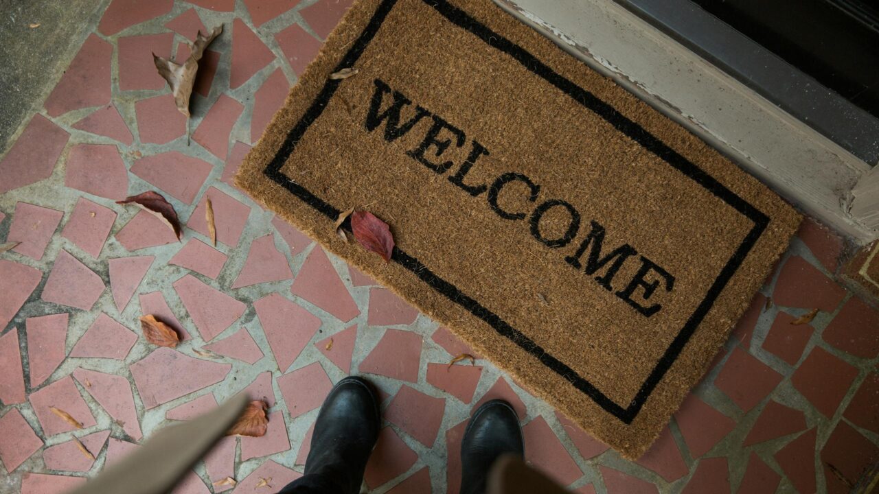 Welcome mat on a tiled porch with boots visible. Perfect for home decor or hospitality themes.